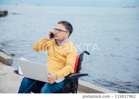 Man Sitting in Wheelchair Working on Laptop Talking on Smartphone Man Sitting in Wheelchair Working on Laptop Talking on Smartphone 119817962