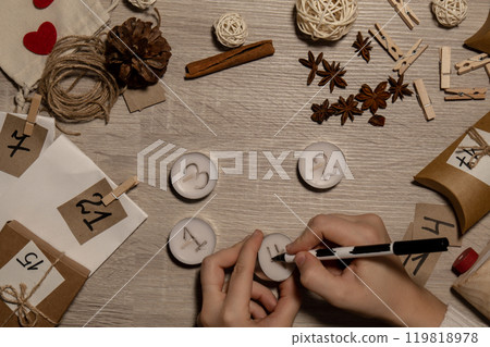 Unrecognizable young woman paint numbers on tea candles. Female making homemade advent calendar Made with your own hands step by step DIY crafts do it yourself. Preparation to christmas concept Unrecognizable young woman paint numbers on tea candles. Female making homemade advent calendar Made with your own hands step by step DIY crafts do it yourself. Preparation to christmas concept 119818978