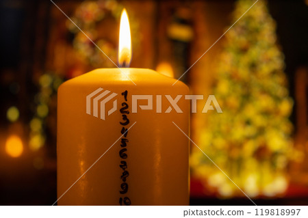 Candle with advent calendar on background of christmas tree lights decorations. Traditional Burning Christmas Wax Candles with numbers counting down for Christmas. Beautiful Advent At Home. Festive 119818997