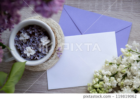 Empty envelope copy space paper note with Tasty black tea in white cup on windowsill with aromatic lilac flowers. Spring composition Cup of lilac tea drinking recipe flowering branches of purple lilac 119819062