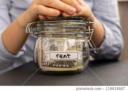 Female hands holding Glass jar full of American currency dollars cash banknote with text RENT. Preparation saving money. Moderate consumption and economy 119819087