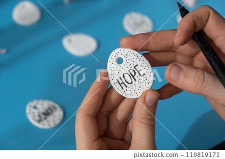 Workshop writing word HOPE on EASTER egg Creator is using white air dry clay for making decor to EASTER holiday. Creating hobby recreation activity that involves fingers. DIY crafting Workshop writing word HOPE on EASTER egg Creator is using white air dry clay for making decor to EASTER holiday. Creating hobby recreation activity that involves fingers. DIY crafting 119819171