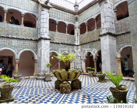 Interior of the arched courtyard with beautifully decorated arches and columns in Arabic style and the yellow painted walls of the Pena Palace in Sintra, Portugal. Interior of the arched courtyard with beautifully decorated arches and columns in Arabic style and the yellow painted walls of the Pena Palace in Sintra, Portugal. 119819182