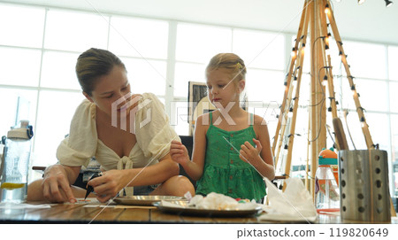 Mother and her daughter paint Halloween cookies  119820649