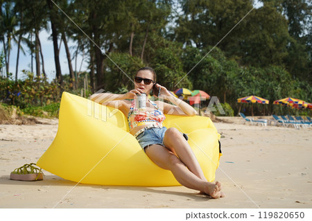 A young woman on the beach lounging on a yellow bean bag A young woman on the beach lounging on a yellow bean bag 119820650