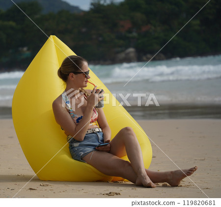 A young woman on the beach lounging on a yellow bean bag  119820681