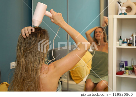 A woman is expertly styling her hair using a blow dryer and brush while in the bathroom 119820860