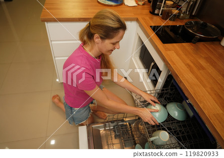 Young woman takes dishes out of the dishwasher machine Young woman takes dishes out of the dishwasher machine 119820933