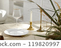 Elegant table setting with candle holders, white plate, and wine glass in natural sunlight 119820997