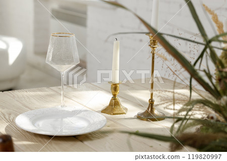 Elegant table setting with candle holders, white plate, and wine glass in natural sunlight 119820997