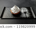 The sand basket is decorated with a high peak of protein cream. A tasty and sweet dessert stands on a black plate on a gray background 119820999