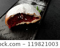 An appetizing donut with strawberries sprinkled with powdered sugar on a black rectangular plate on a gray background 119821003