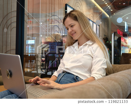 A young woman enjoys coffee while working on her laptop  119821133