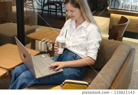 A young woman enjoys coffee while working on her laptop  119821143