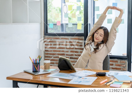 Tired young businesswoman stretching her arms and upper body while sitting at her office desk Tired young businesswoman stretching her arms and upper body while sitting at her office desk 119821343