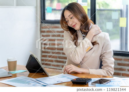 Tired young businesswoman using one hand to massage her shoulder to ease the neck and shoulder pain from long working hours 119821344