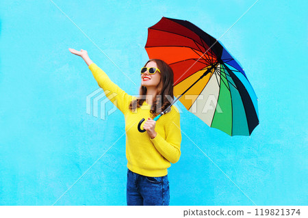Happy smiling woman holding colorful umbrella in autumn day looking up on colorful blue background 119821374