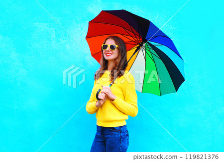 Happy smiling young woman holding colorful umbrella in autumn day on blue background 119821376