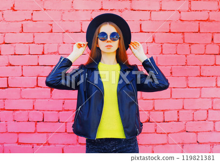 Fashion young woman wearing a black hat, jacket on colorful pink bricks background 119821381