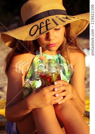 Beautiful swarthy teenage girl wearing straw hat with Offline text holding plastic glass of cool lemonade on summer day. Portrait of a mysterious baby female tin kid on summer vacation. Children's Day Beautiful swarthy teenage girl wearing straw hat with Offline text holding plastic glass of cool lemonade on summer day. Portrait of a mysterious baby female tin kid on summer vacation. Children's Day 119822106