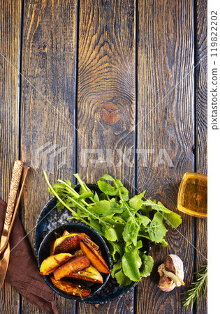Baked potato wedges with addition sea salt and rucola on wooden background Baked potato wedges with addition sea salt and rucola on wooden background 119822202