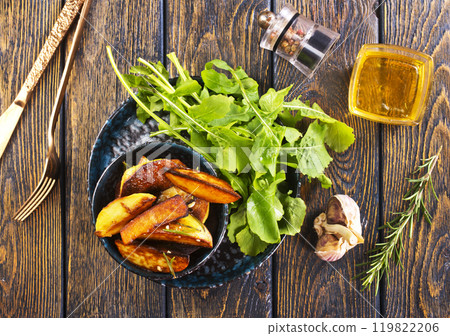 Baked potato wedges with addition sea salt and rucola on wooden background Baked potato wedges with addition sea salt and rucola on wooden background 119822206