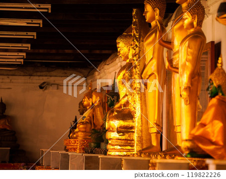 Golden Buddha statues line a row in a Thai temple. 119822226