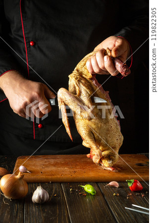 A chef carves a bird, demonstrating his skills in a rustic kitchen. Ingredients such as onions and garlic surround a wooden cutting board, enhancing the culinary atmosphere A chef carves a bird, demonstrating his skills in a rustic kitchen. Ingredients such as onions and garlic surround a wooden cutting board, enhancing the culinary atmosphere 119822305