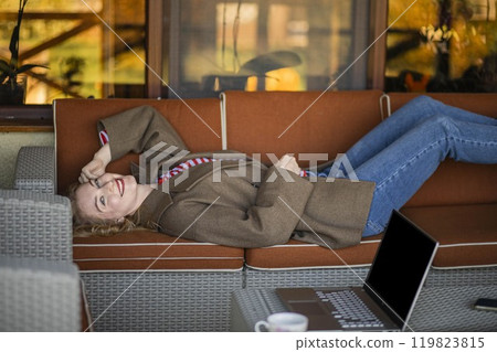 Balance productivity with relaxation to enhance creativity and performance. freelance woman lies on sofa outdoors, laptop 119823815