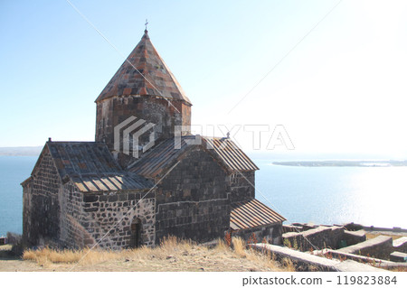 Ancient stone church overlooking a scenic lake with a bright sky. 119823884