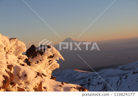 Breathtaking view of a snowy mountain peak surrounded by rocky terrain and clear blue skies at dawn Breathtaking view of a snowy mountain peak surrounded by rocky terrain and clear blue skies at dawn 119824177