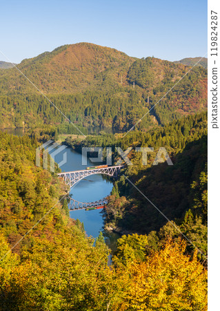 Mountains covered in autumn leaves and a locomotive crossing the Tadami River Bridge 119824287