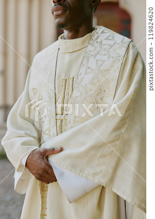 Vertical shot of unrecognizable priest dressed in golden white robe crossed his hands while standing outside Vertical shot of unrecognizable priest dressed in golden white robe crossed his hands while standing outside 119824620