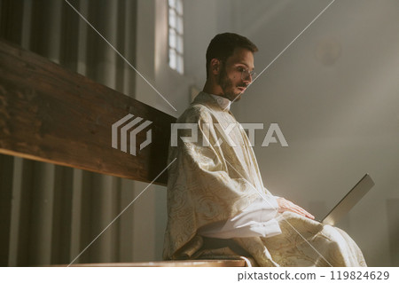 Young Caucasian priest dressed in golden white robe surfing Internet while sitting in church 119824629