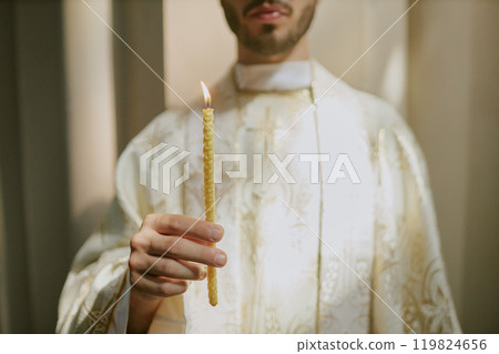 Medium close up of unrecognizable priests hand holding thin candle during church service 119824656