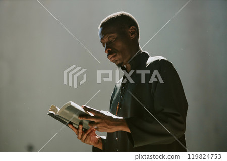 Low angle shot of African American priest reading holy book under sunrays in church 119824753