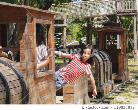 Children play outdoors on a wooden playground in a park. Happy girl playing with wooden train in playground during summer. 119825932