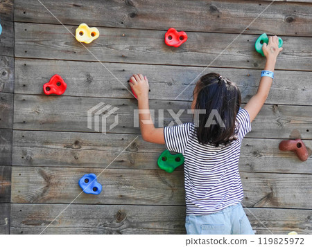 Children play outdoors on a wooden playground in a park. Happy girl playing on wooden climbing wall in playground during summer. Children play outdoors on a wooden playground in a park. Happy girl playing on wooden climbing wall in playground during summer. 119825972