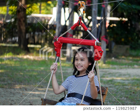Kids play outdoors on a playground with modern slides, rope net bridges, climbing swings, climbers in summer. 119825987