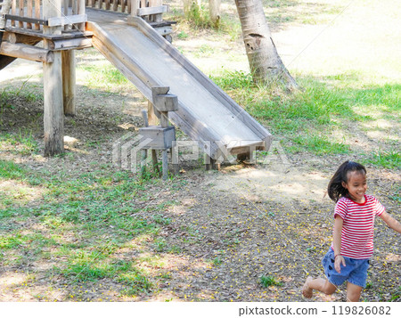 Children play outdoors on a wooden playground in a park. Happy girl playing on slide in playground in summer. 119826082