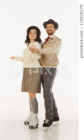 Stylish couple, man and woman wearing retro-styled clothes and headwear, dancing on ice rink, having fun and enjoying cozy date 119826279