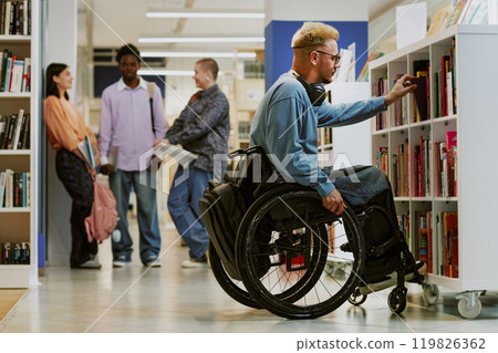 Person in a wheelchair browsing books at a modern library, with diverse group of people engaging in background activities shelving books and discussing literature Person in a wheelchair browsing books at a modern library, with diverse group of people engaging in background activities shelving books and discussing literature 119826362