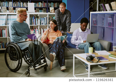 Group of diverse students collaborating in modern library environment discussing projects, sharing ideas seated on sofas and using laptops for studying, learning together 119826381