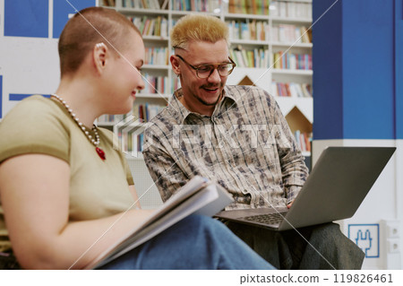 Two people sitting in study space working together on a laptop. Engaging in discussion and exchanging notes in a library setting 119826461
