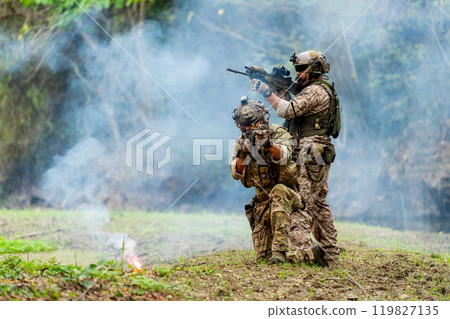 Militaries or soldiers stay in battlefield near the river with one sit down and one stand and point gun forward direction and in front of flare firework during outdoor practice. 119827135
