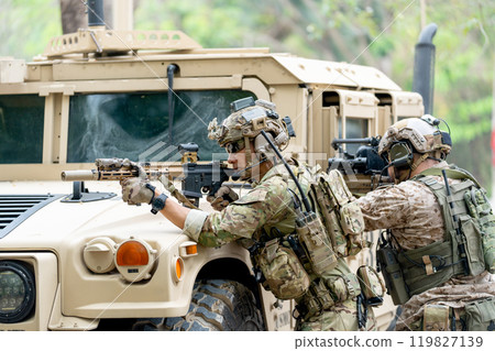 Wide shot of two militaries or soldiers stay in front of humvee car area of car hood and point gun to left side during outdoor practice. 119827139