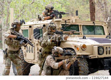 Group of militaries or soldiers stay near humvee car with one on roof and the other stay in area of car hood also point gun to right side during outdoor practice. 119827144