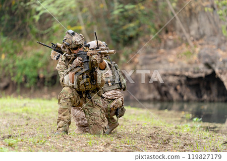Two militaries or soldiers stay in battlefield near the river with sit down and point gun in different direction during outdoor practice. 119827179