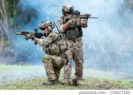Militaries or soldiers stay in battlefield near the river with one sit down and one stand and point gun forward direction during outdoor practice. 119827180