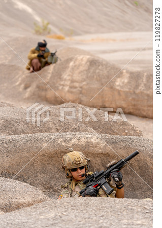 Vertical image military or soilder man hold gun and sit in the pit or slope in front of the terrorist who stay in back of battlefield in area near mountain. 119827278